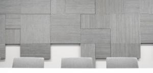 Three gray chairs are aligned in front of a wall adorned with textured, geometric acoustic panels in varying shades of gray, creating a modern and minimalist aesthetic.