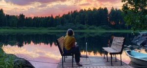 Ihminen istuu laiturin penkillä ja katselee auringonlaskua järven yli.
